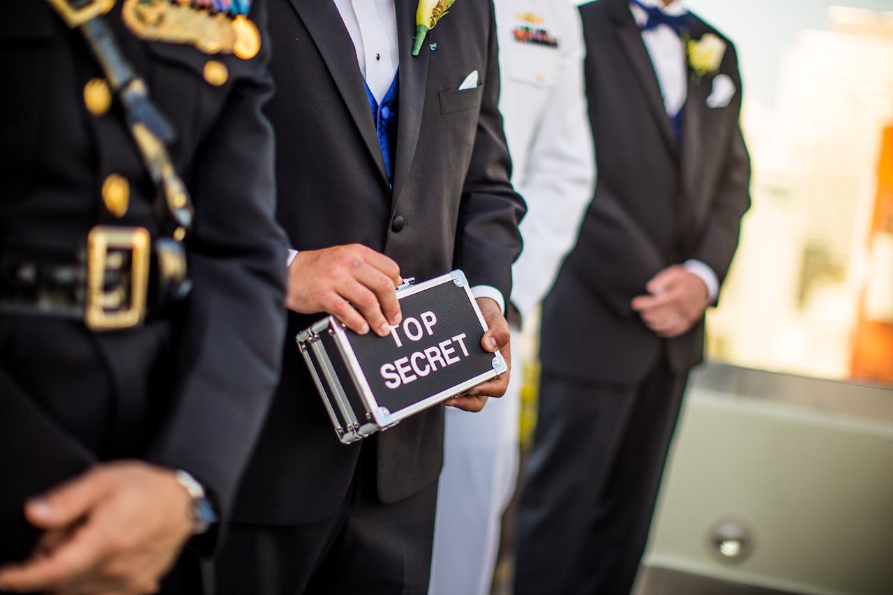 services-01 A group of men in formal military and business attire holding a 'Top Secret' briefcase indoors.
